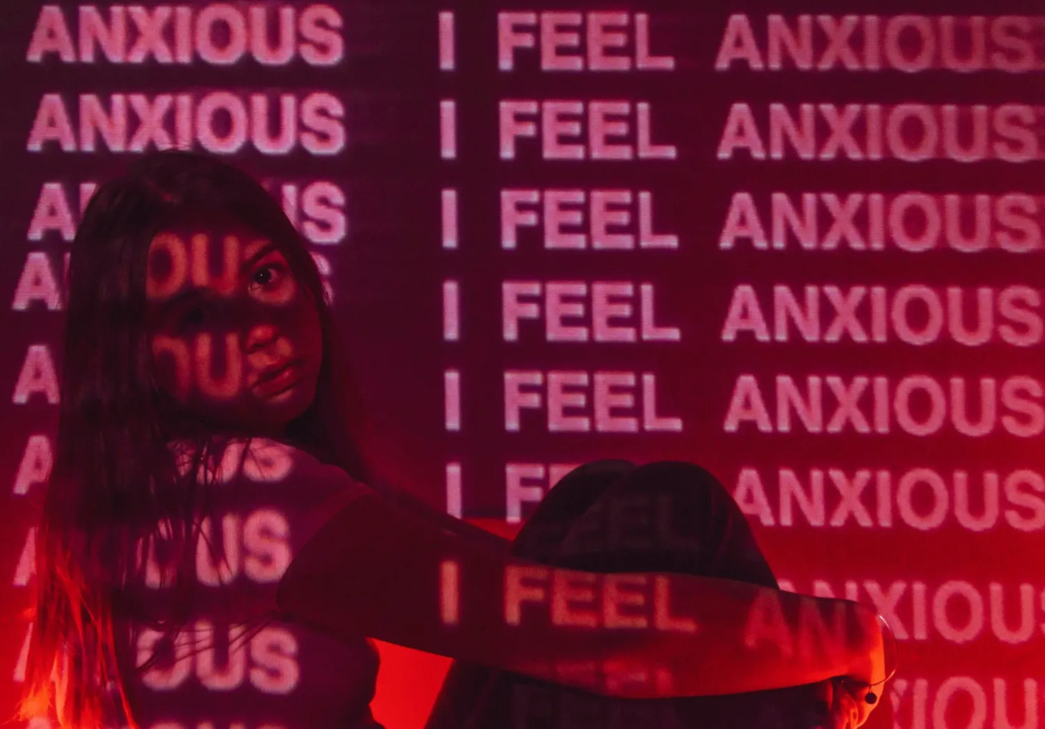 A young girl holding her knees with I Feel Anxious covering the entire picture