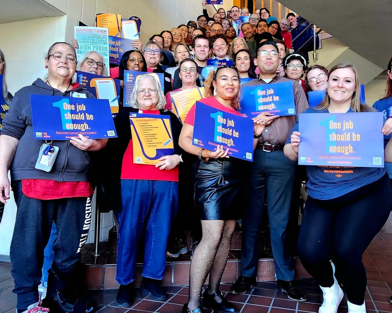 KNEA ESP members pose for a picture together holding signs that say, "1 job should be enough."